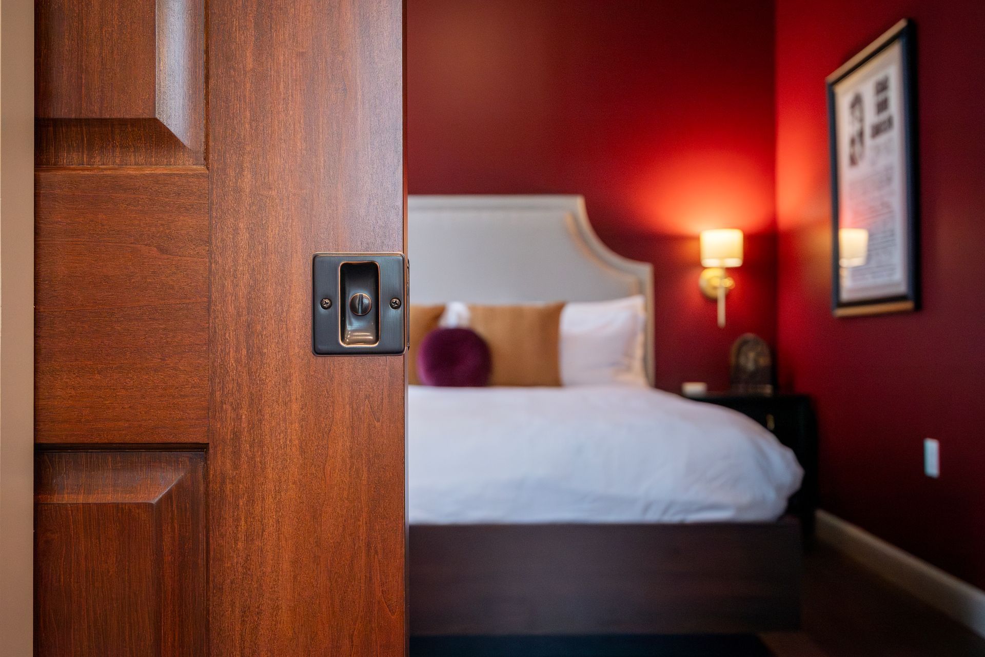 Door partially open, revealing a red-walled bedroom with a bed, lamps, and a framed picture.