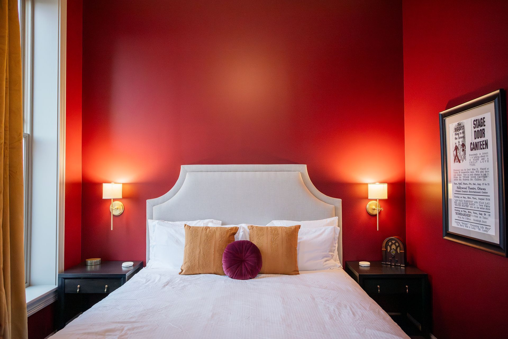 Bedroom with red walls, white bed, gold pillows, nightstands, and framed artwork.