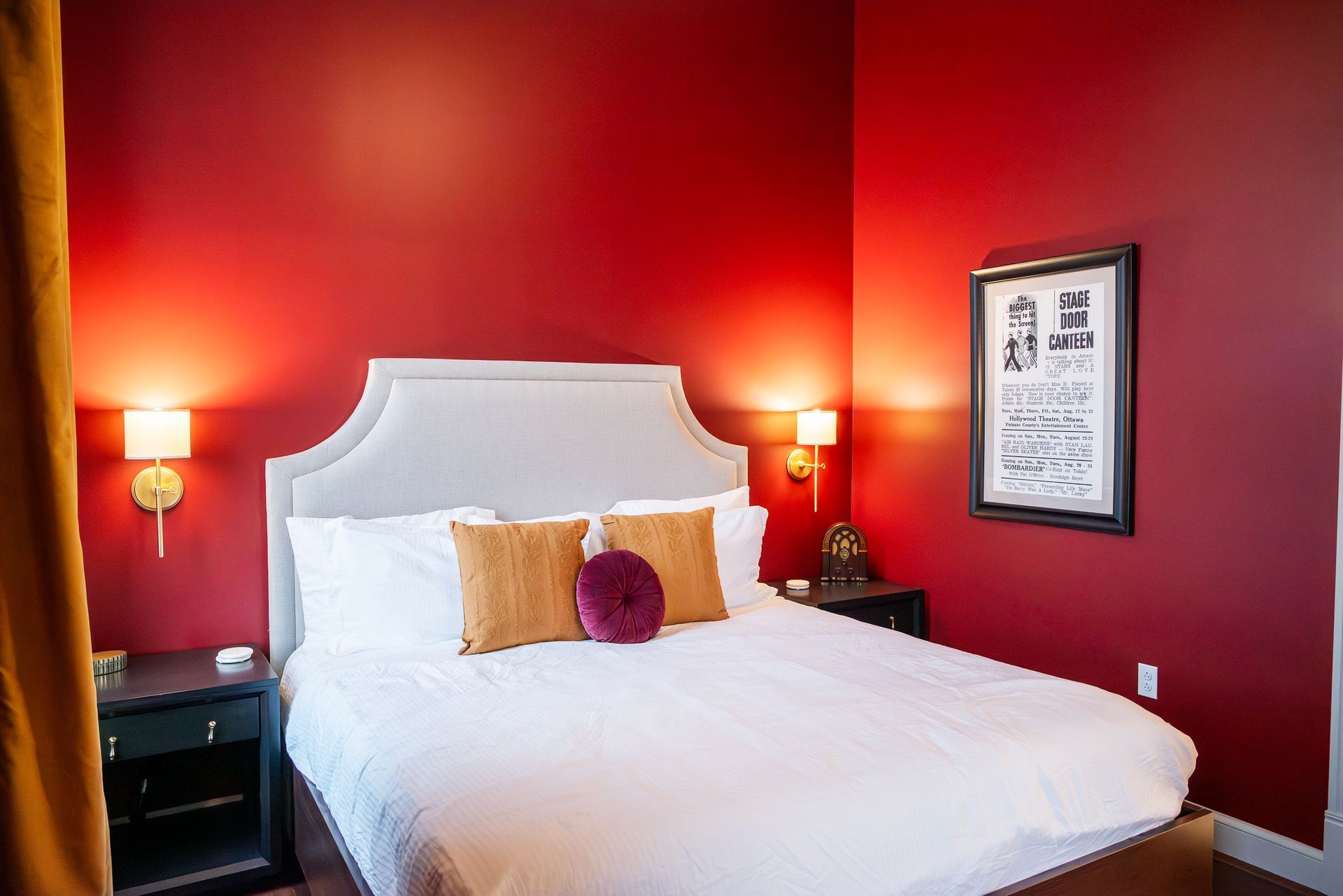 Red bedroom with a bed, two nightstands, two wall sconces, and a framed print.