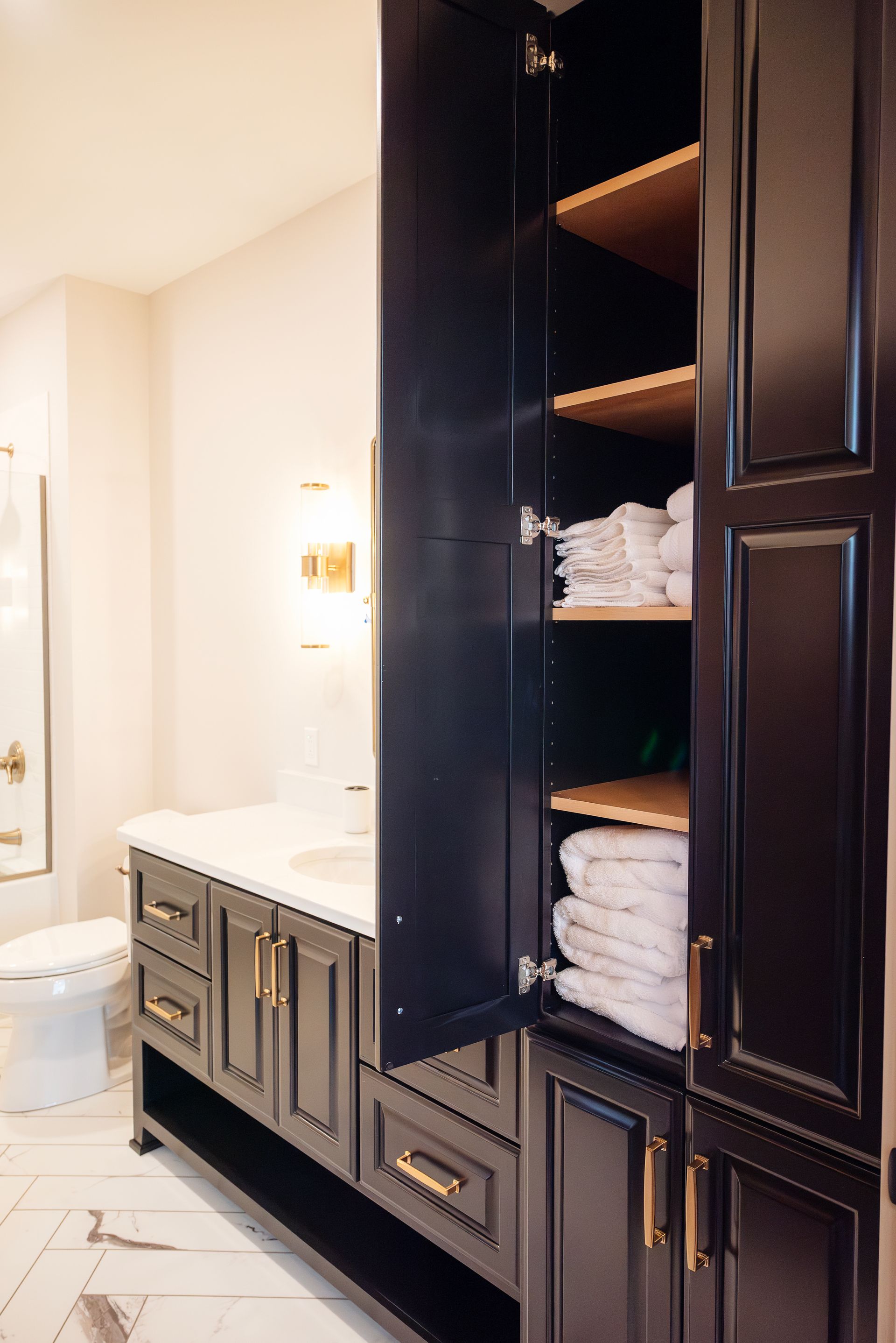 Dark blue bathroom cabinet with open door, shelves with towels, white towels, gold hardware.