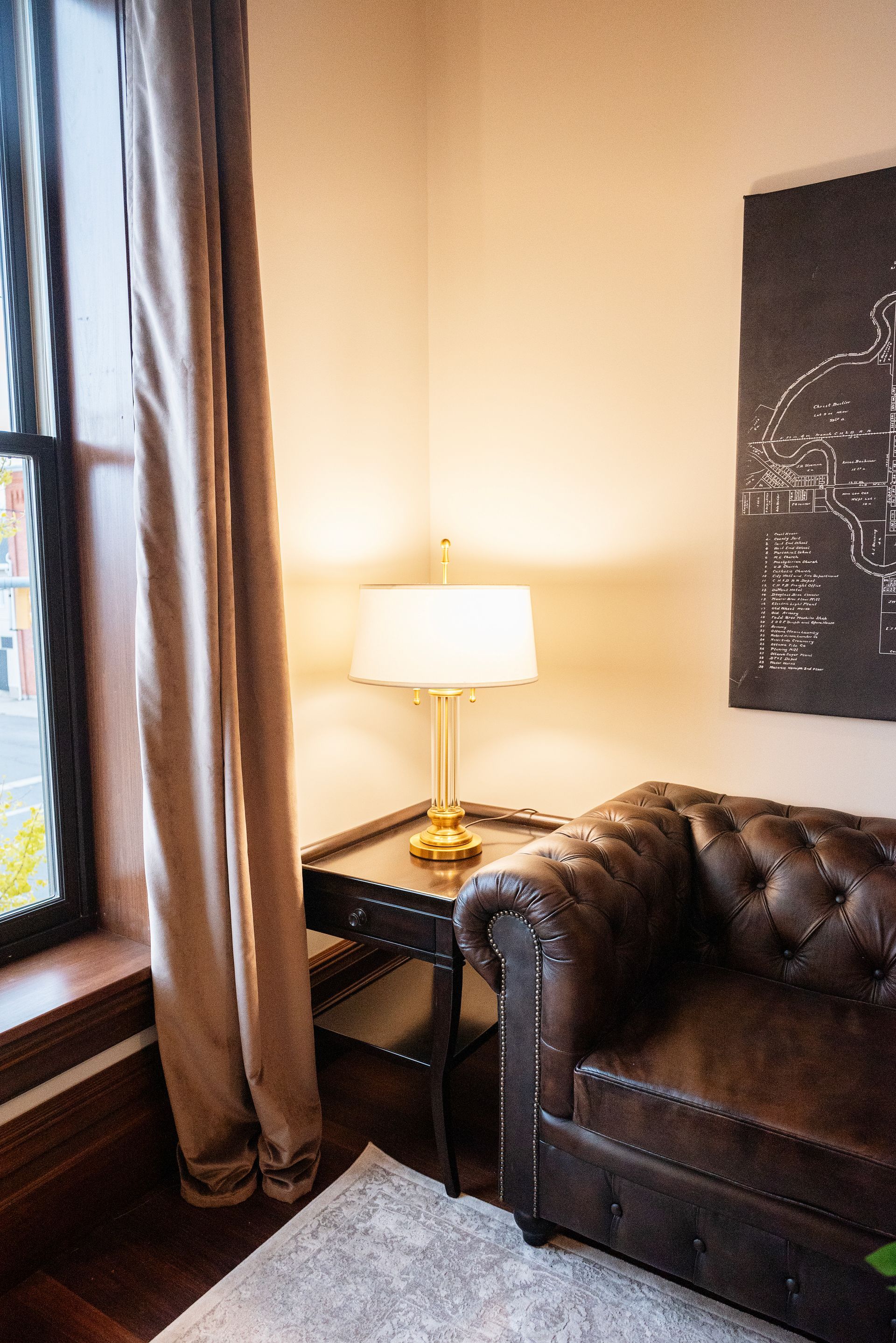 Brown leather armchair, lamp on a side table, window with curtain.
