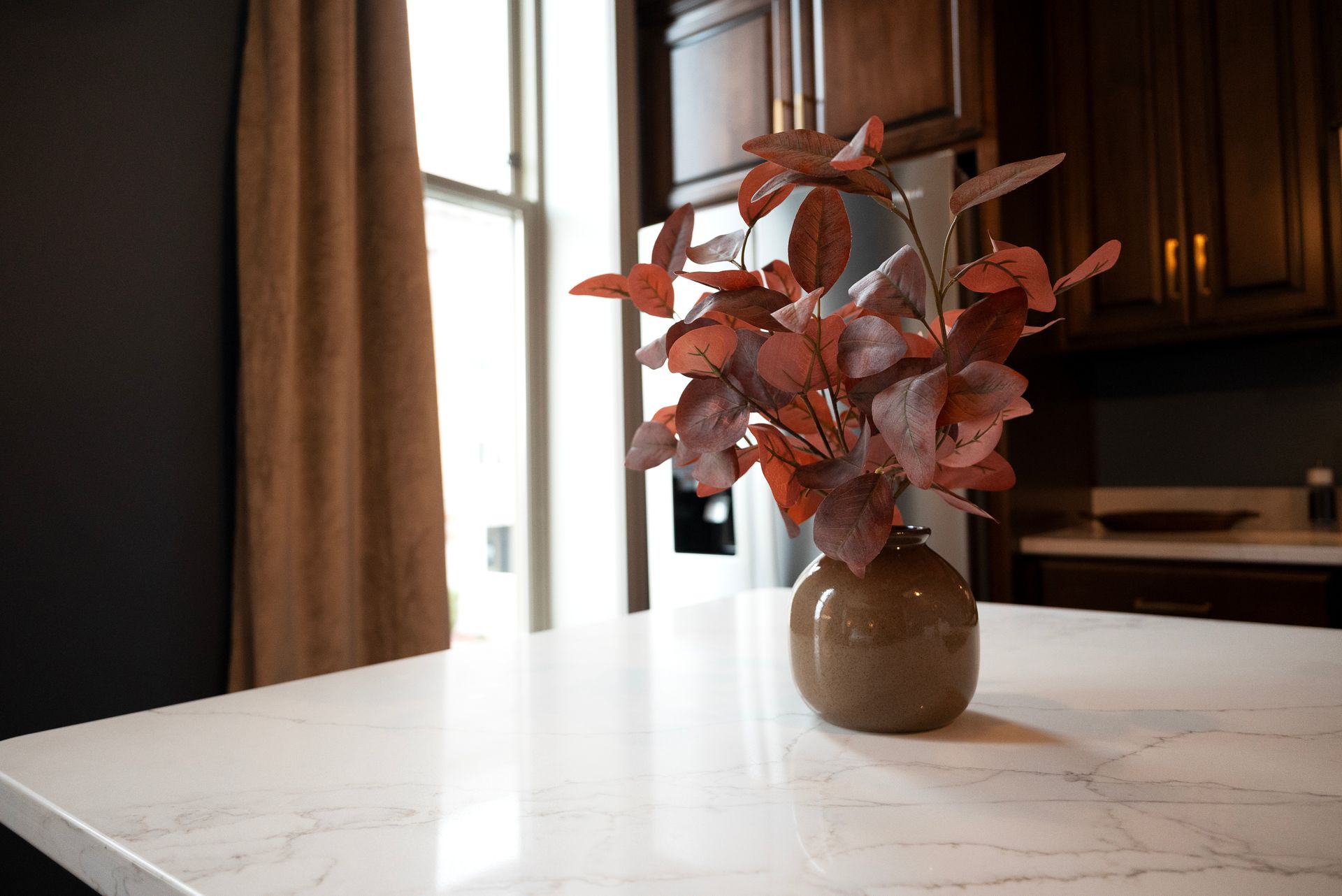 A brown vase with red leaves on a white countertop in a kitchen.