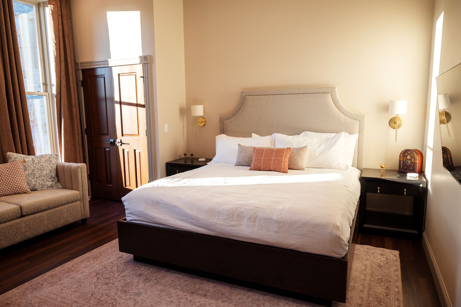 Bedroom with bed, small sofa, wood floors, and sunlight.