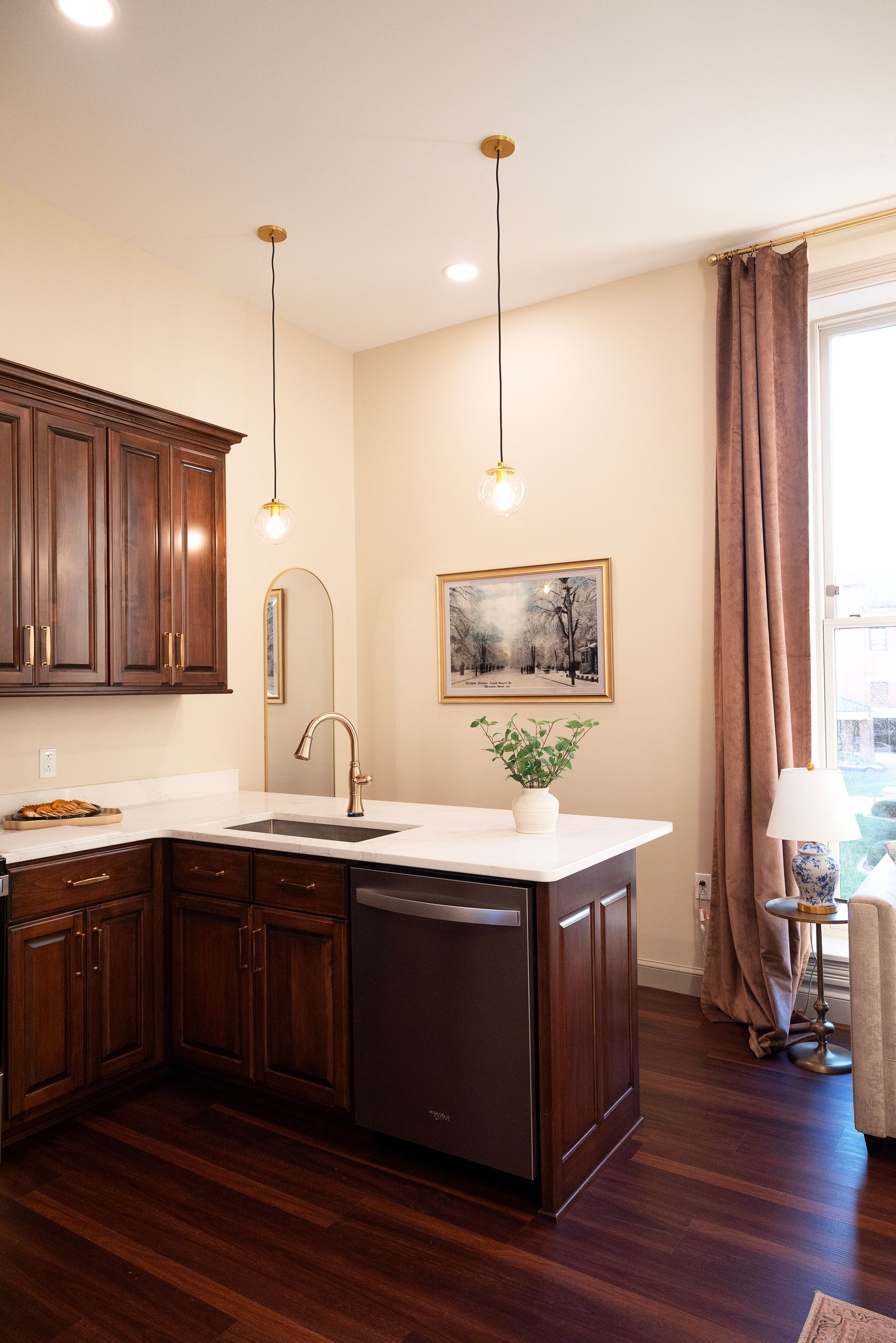 Dark wood kitchen with white countertops, stainless steel appliances, and gold pendant lights.
