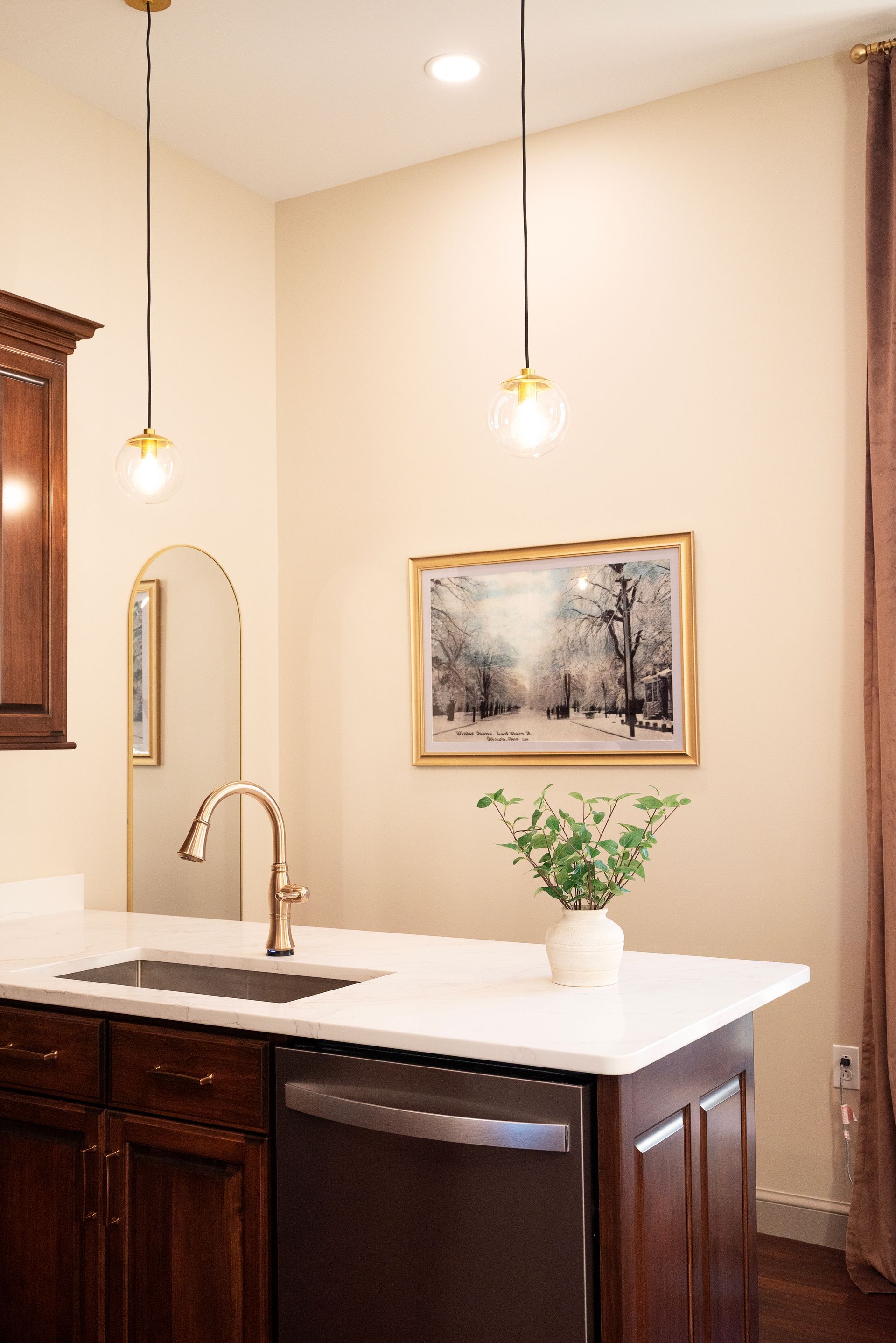 Kitchen with a dark wood island, white countertop, sink, and gold pendant lights.