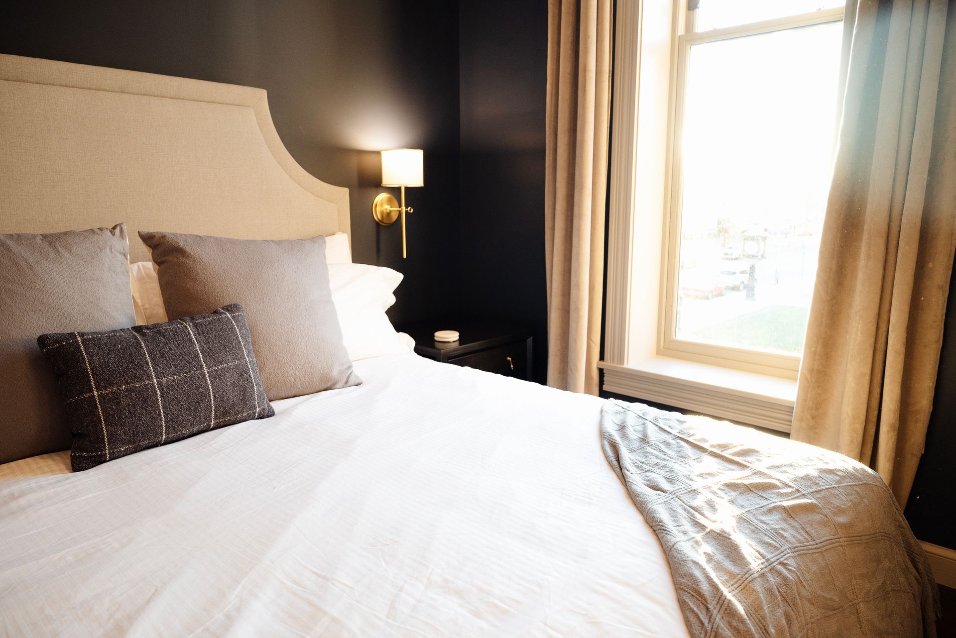 Bedroom with a bed, pillows, and a window with tan curtains.