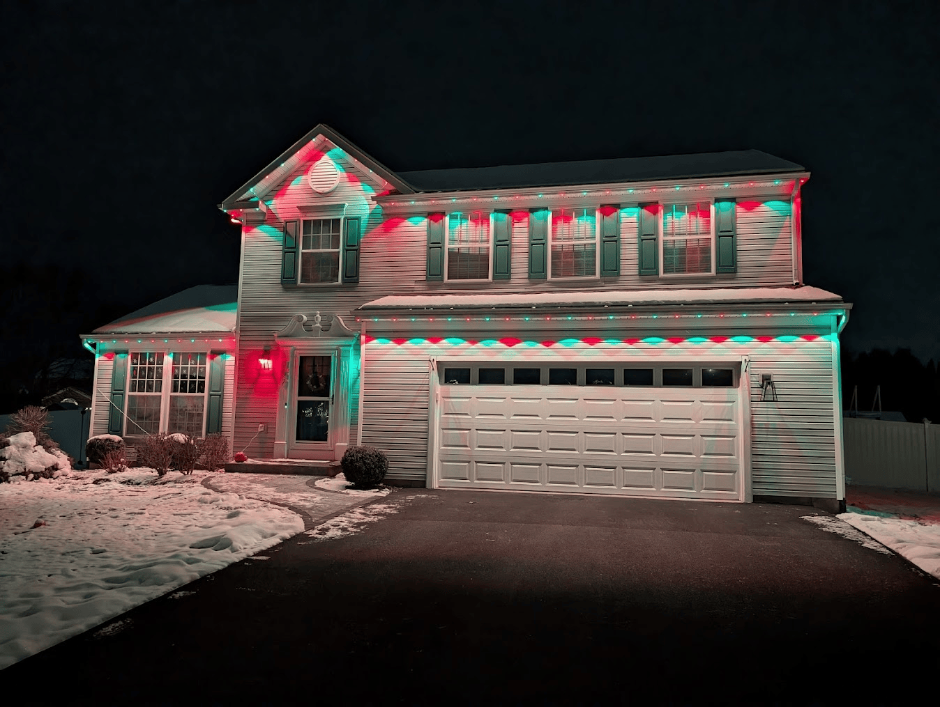 A house is decorated with red and green christmas lights at night.