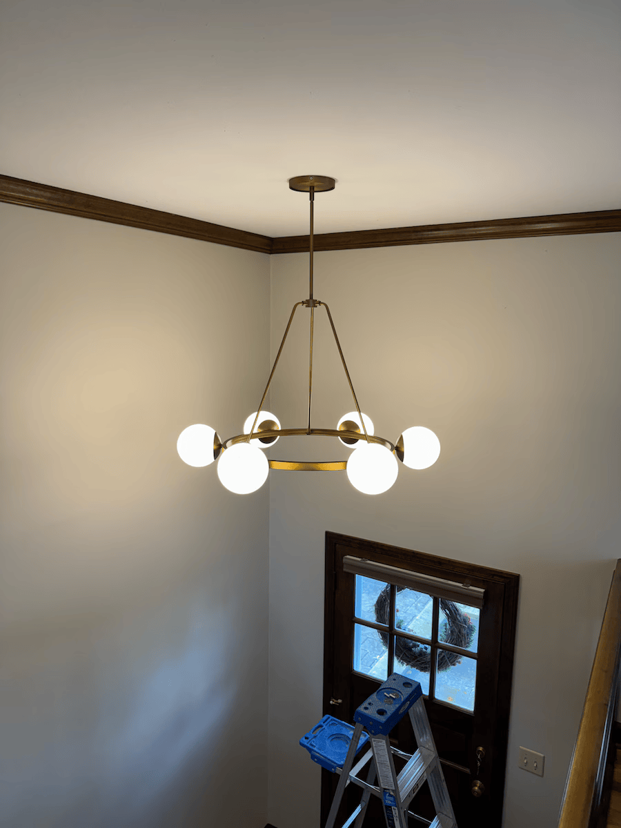 A chandelier is hanging from the ceiling in a room next to a ladder.