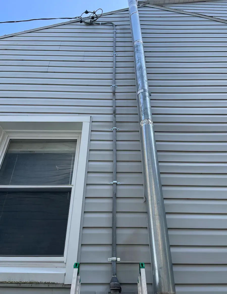 A pipe is attached to the side of a house next to a window.