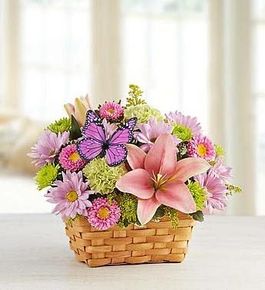 A basket filled with pink flowers and a purple butterfly on a table.