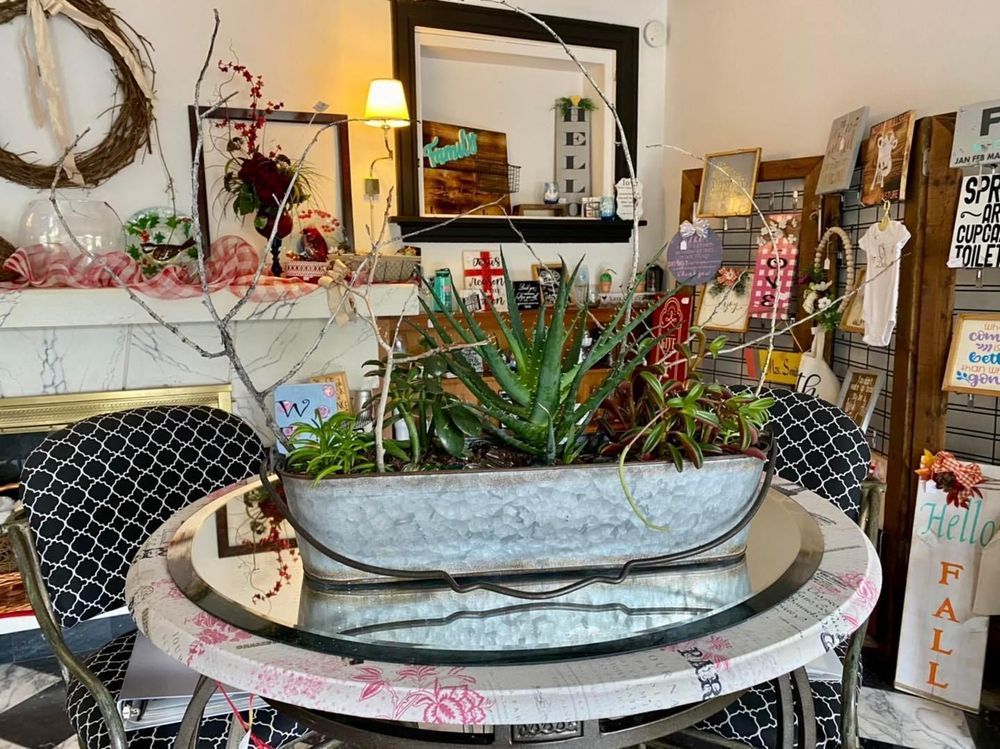 A floral arrangement on a mirrored table in a shop with eclectic decor and a fireplace in the background.