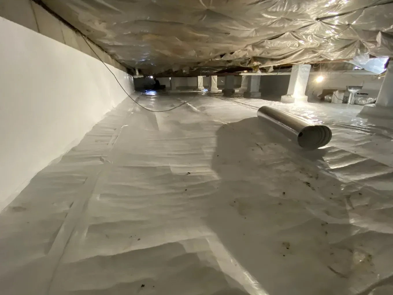 Crawl space with white vapor barrier covering the ground and walls. Ductwork and supports visible.