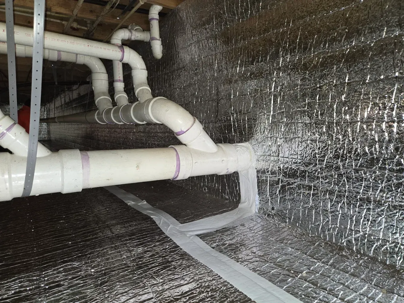 White PVC pipes with insulation in a crawl space.