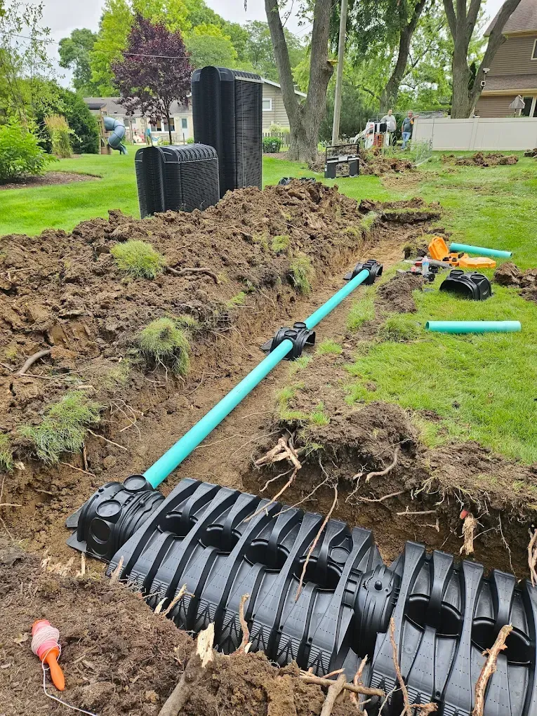 Installation of a subsurface drainage system in a yard. Trenches, pipes, and tanks visible.