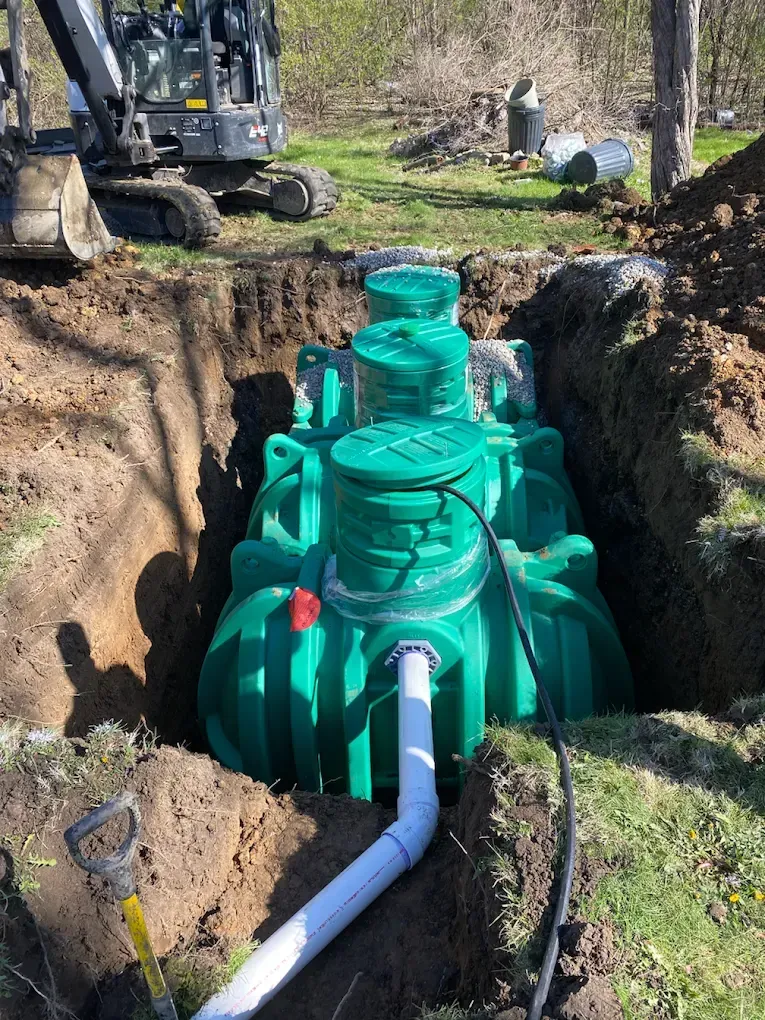Green septic tank in excavated hole, with excavator in background.
