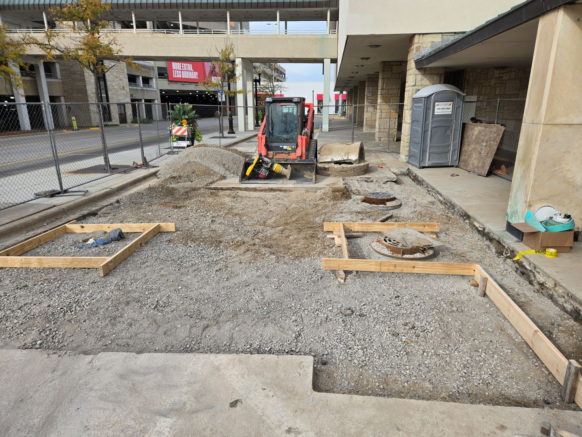 Sidewalk construction site with a small excavator. Wooden frames outline areas.