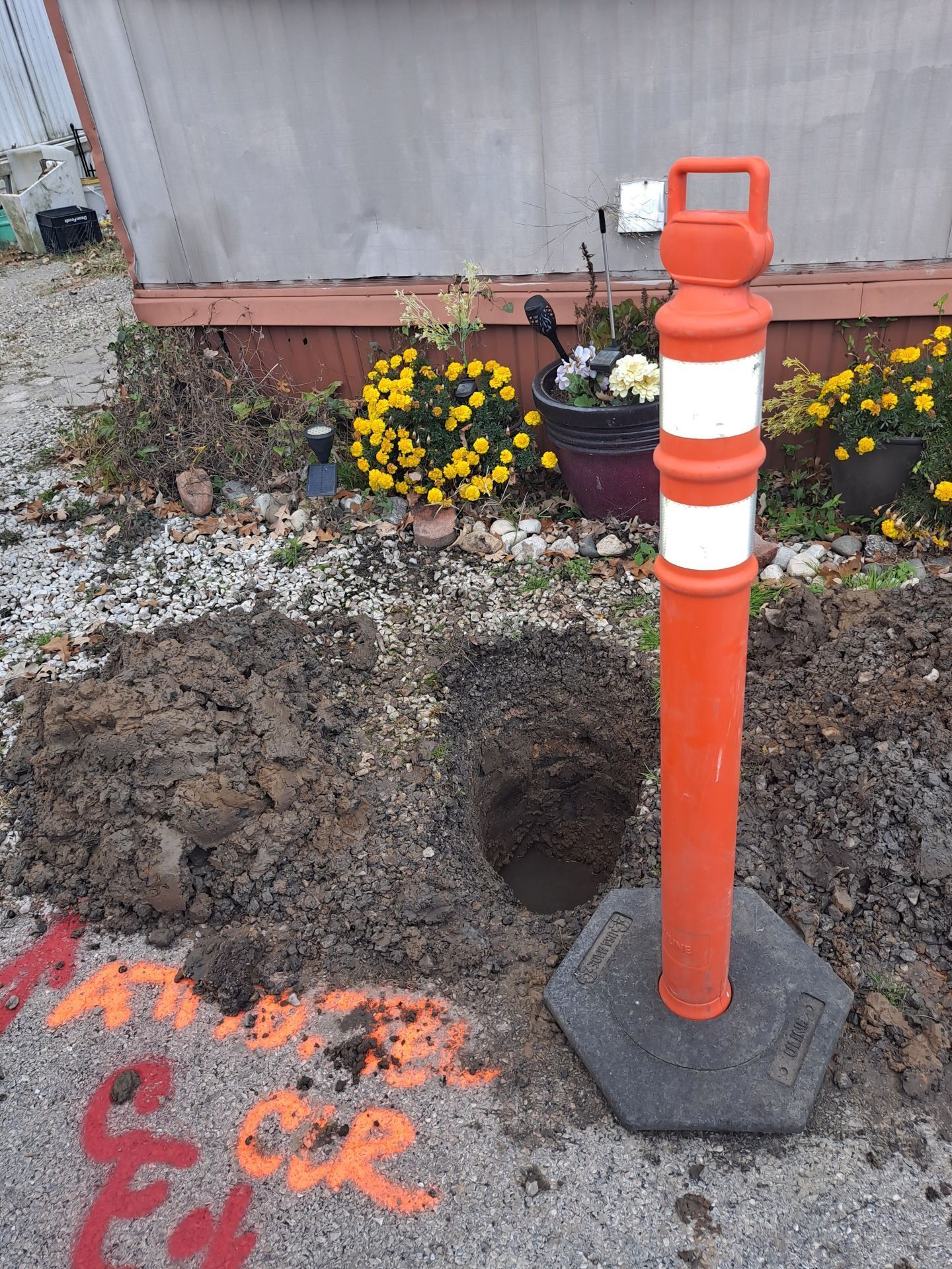 Orange and white bollard next to a newly dug hole in the ground with orange spray paint markings.