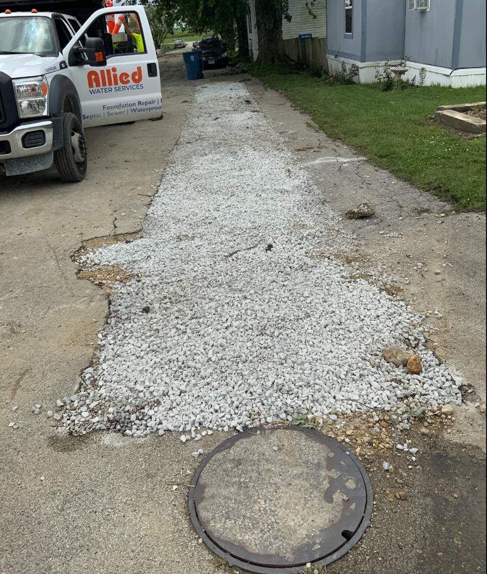 Road repair: gravel over broken pavement, Allied truck, manhole cover, grassy area.
