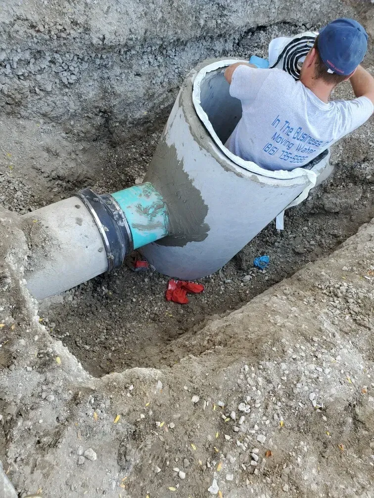 Person inside a concrete pipe, working on a construction project in a trench.