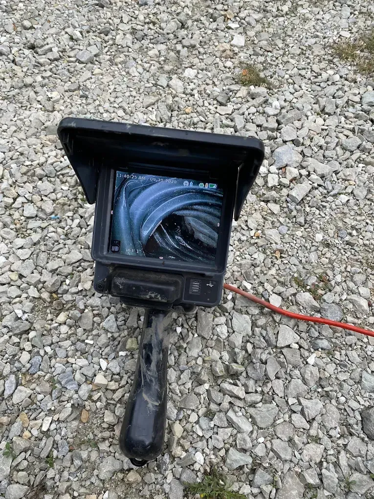 Monitor displaying a view of a pipe, attached to a black handle, on a rocky ground.