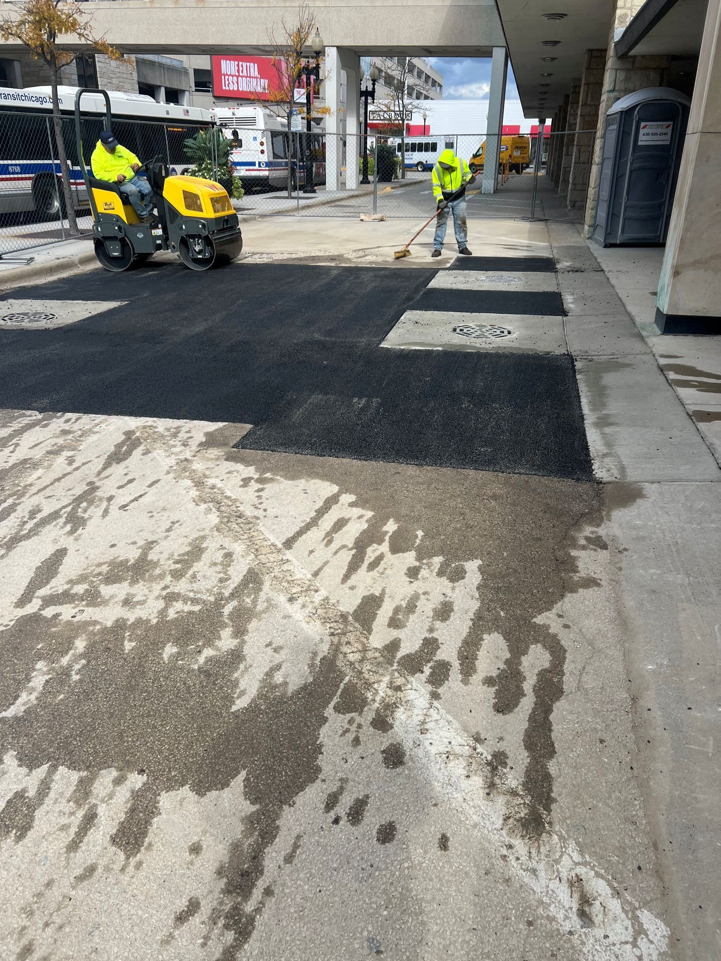 Street resurfacing: Workers with equipment paving asphalt, wet concrete, building background.