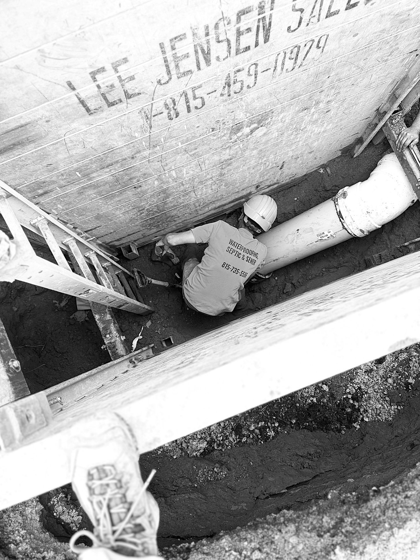 A worker in a ditch with a large pipe, next to a ladder. Wood structure with 