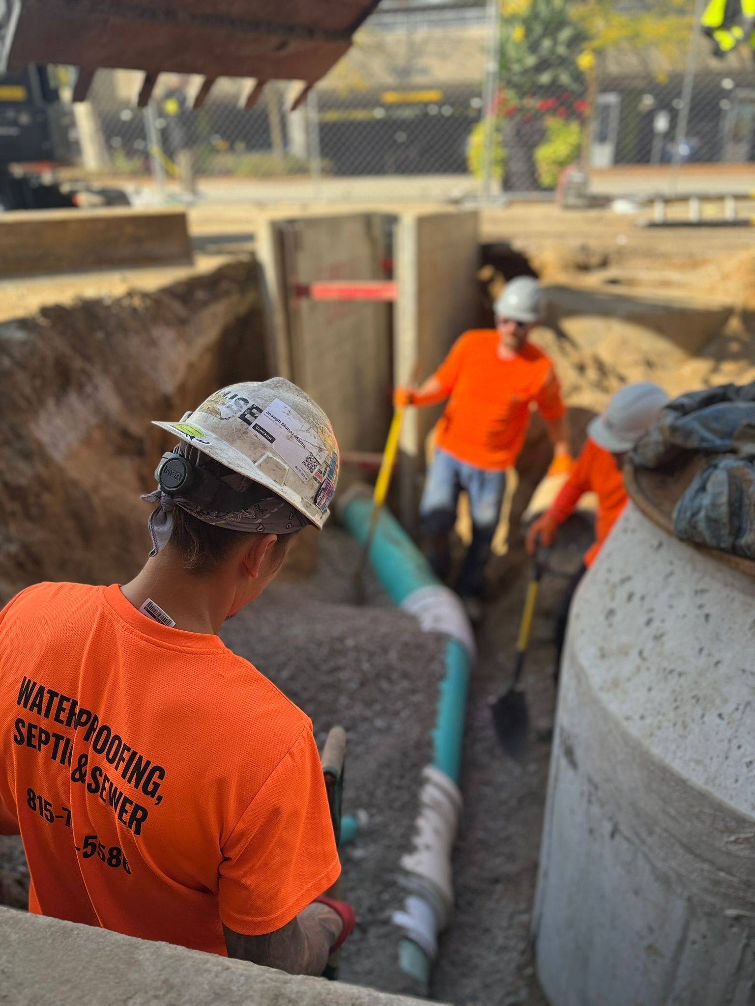Construction workers in orange shirts laying pipe in a trench.