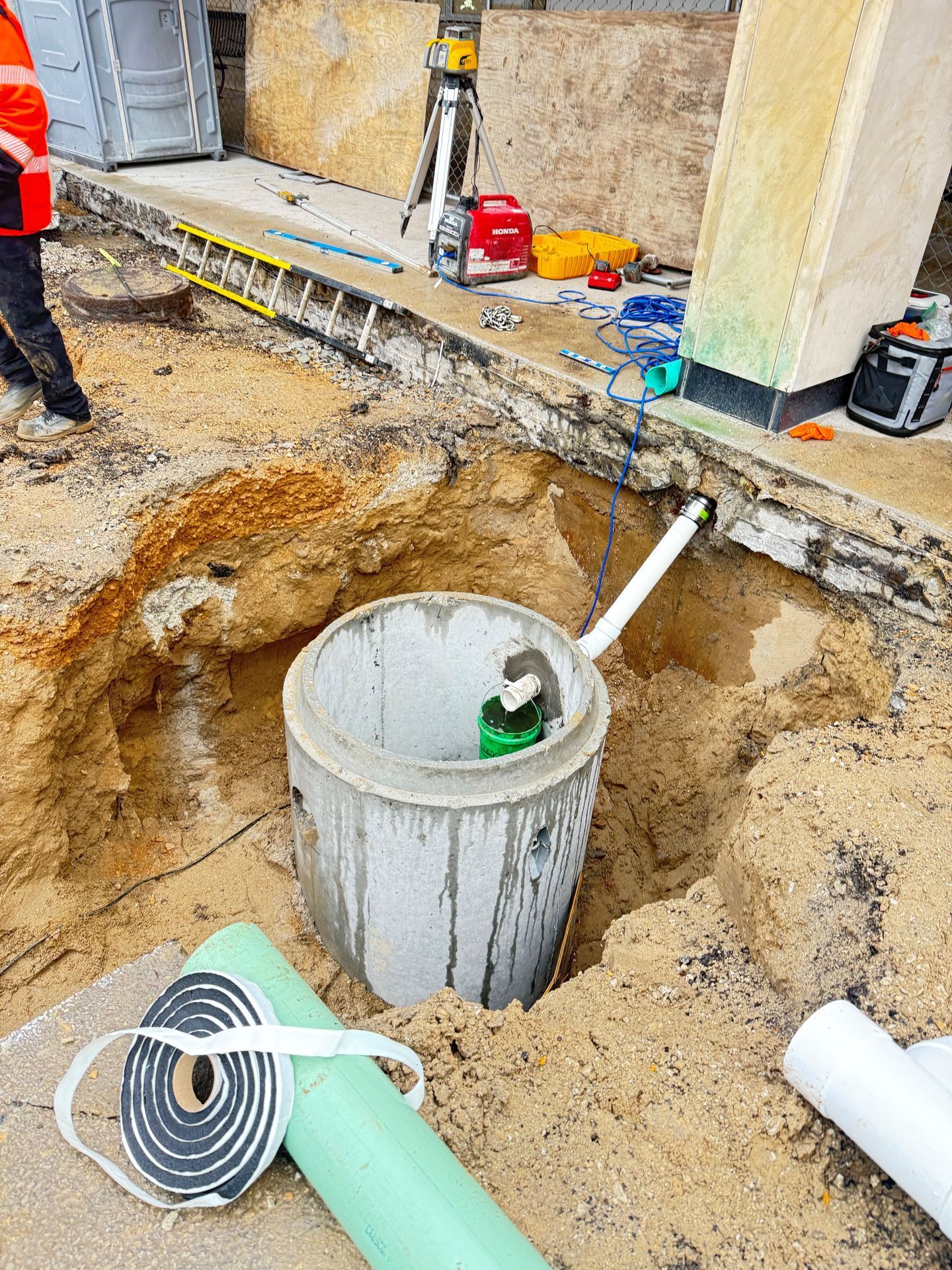 Construction site with an excavated concrete cylinder, pipes, tools, and a worker.