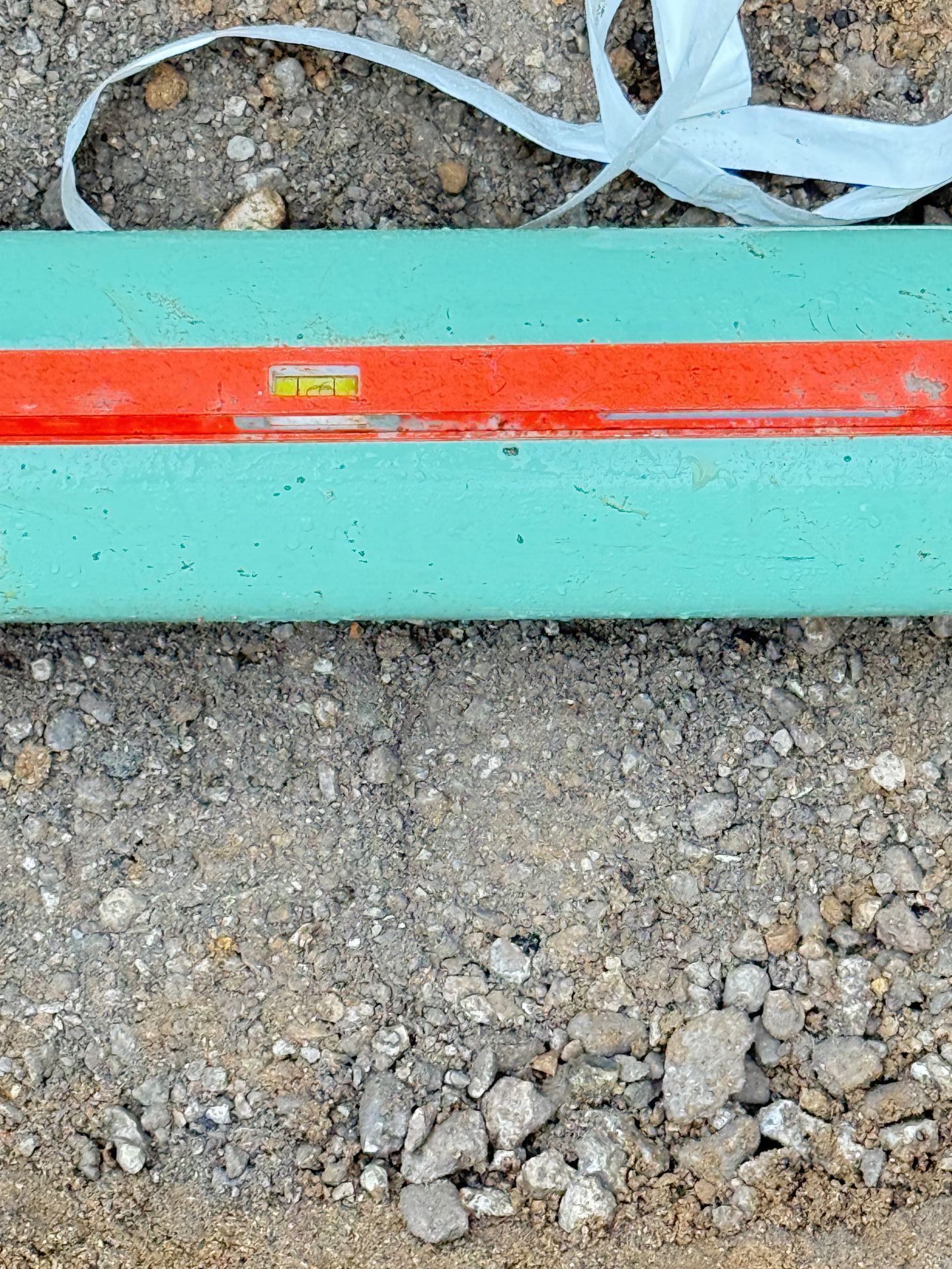 Green pipe on dirt, with a red level placed on top, indicating it is level.