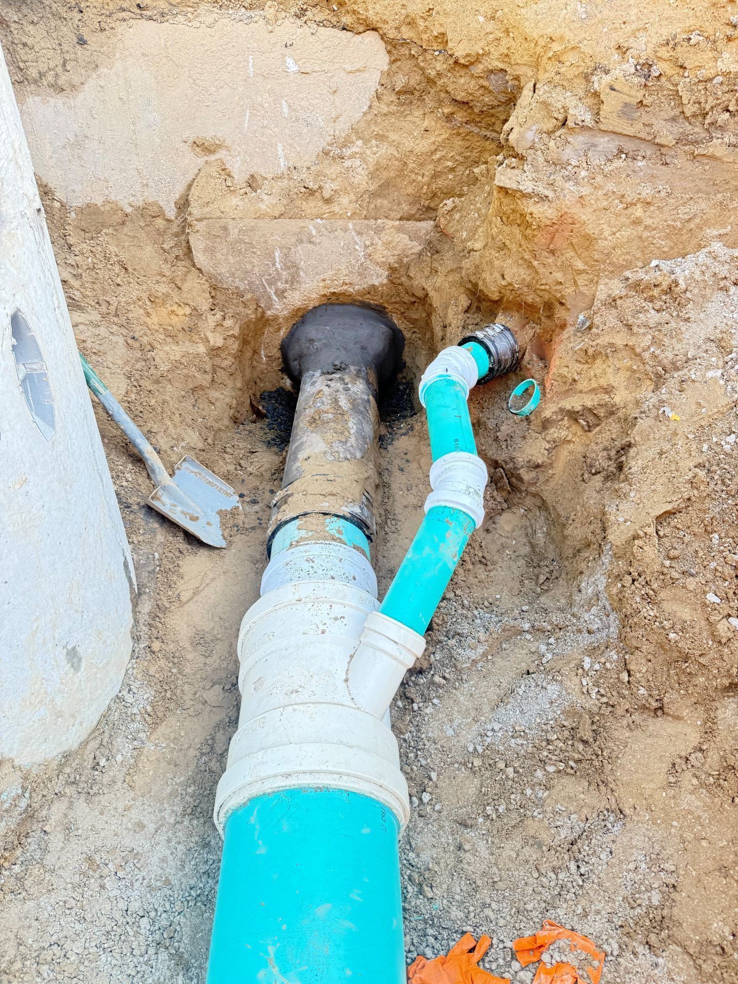 A blue PVC pipe with various fittings emerges from the ground in an excavation.