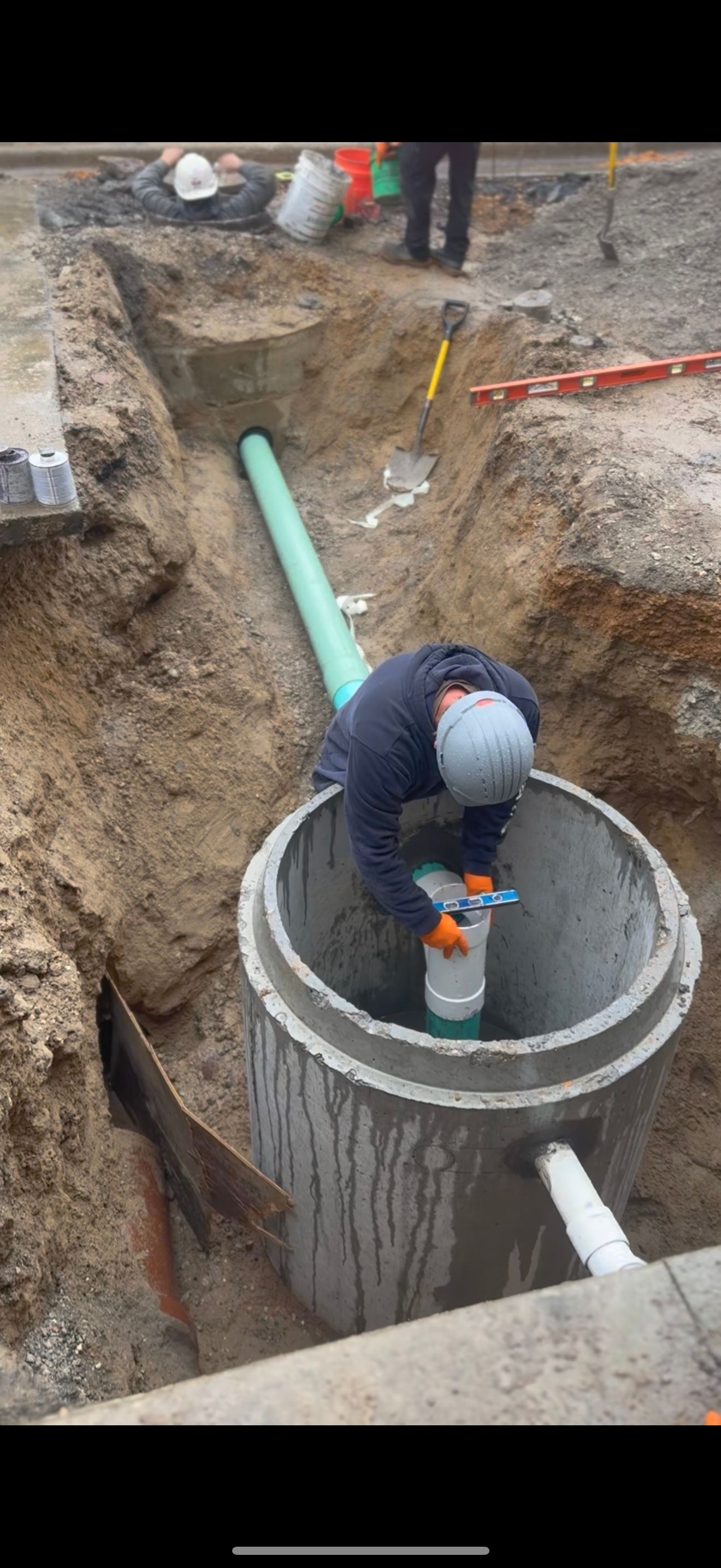Construction worker installing pipes inside a concrete access chamber in an excavation.
