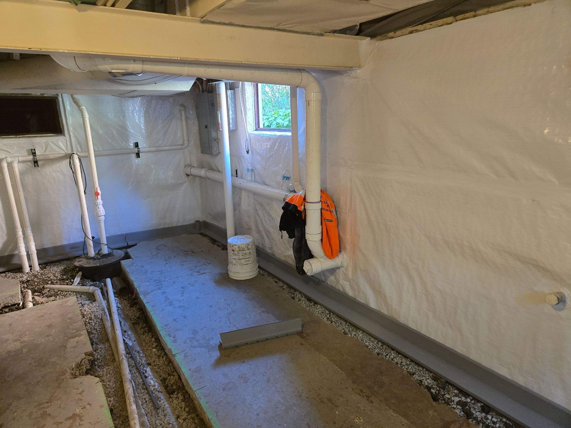 Basement interior with white waterproof barrier, pipes, and sump pump. Cement floor.