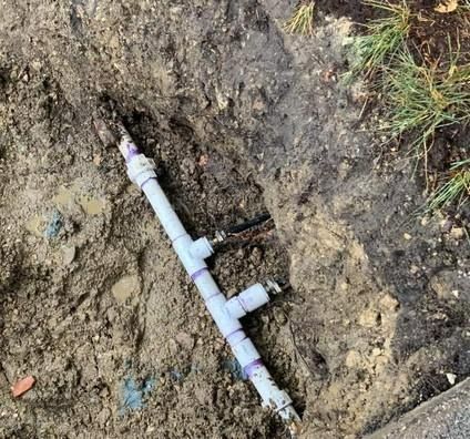 White PVC pipe with fittings in a muddy trench, near grass.