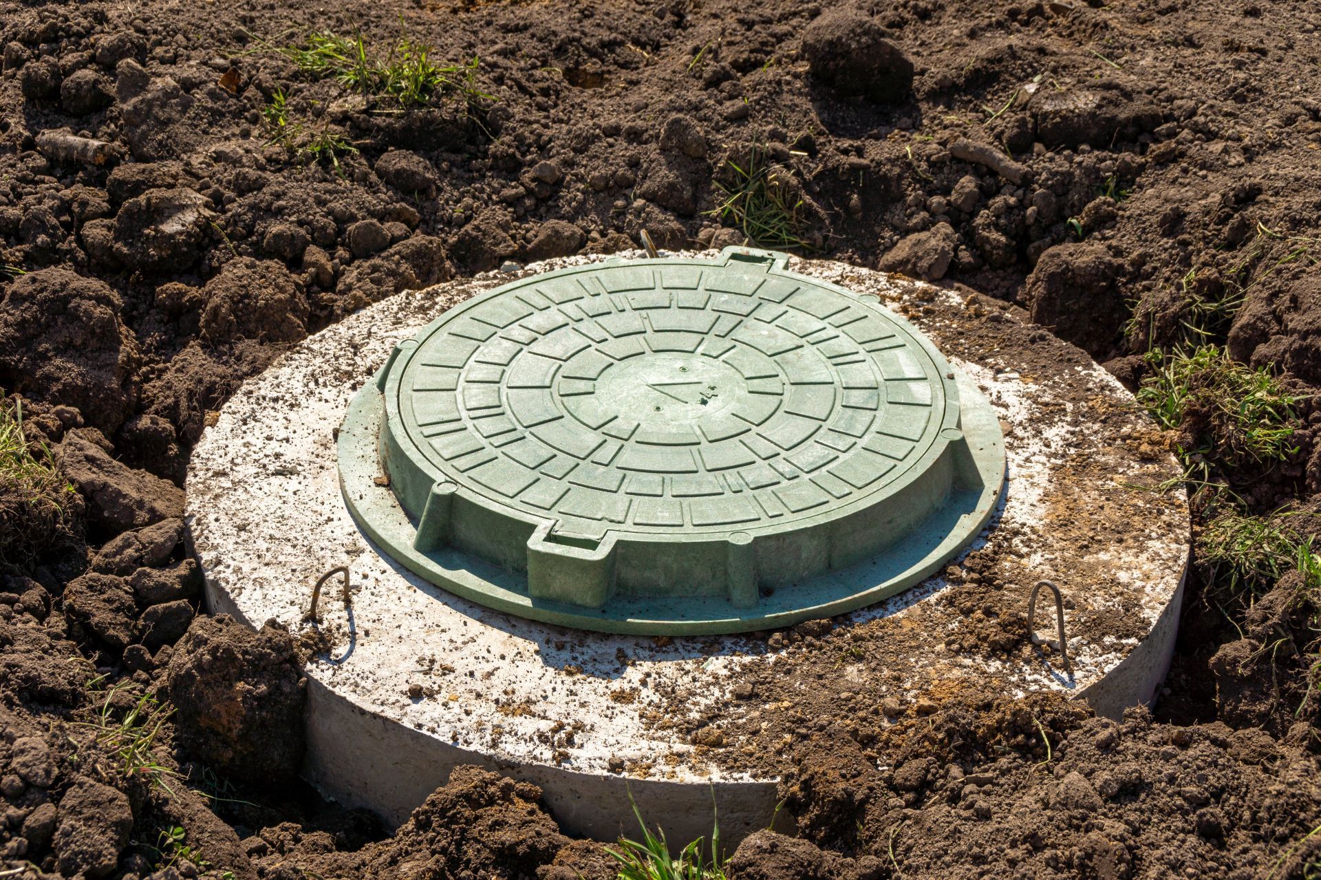 Green septic tank in excavated hole, with excavator in background.
