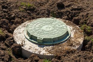 Green septic tank in excavated hole, with excavator in background.