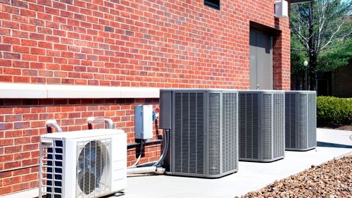 A row of air conditioners are sitting outside of a brick building.