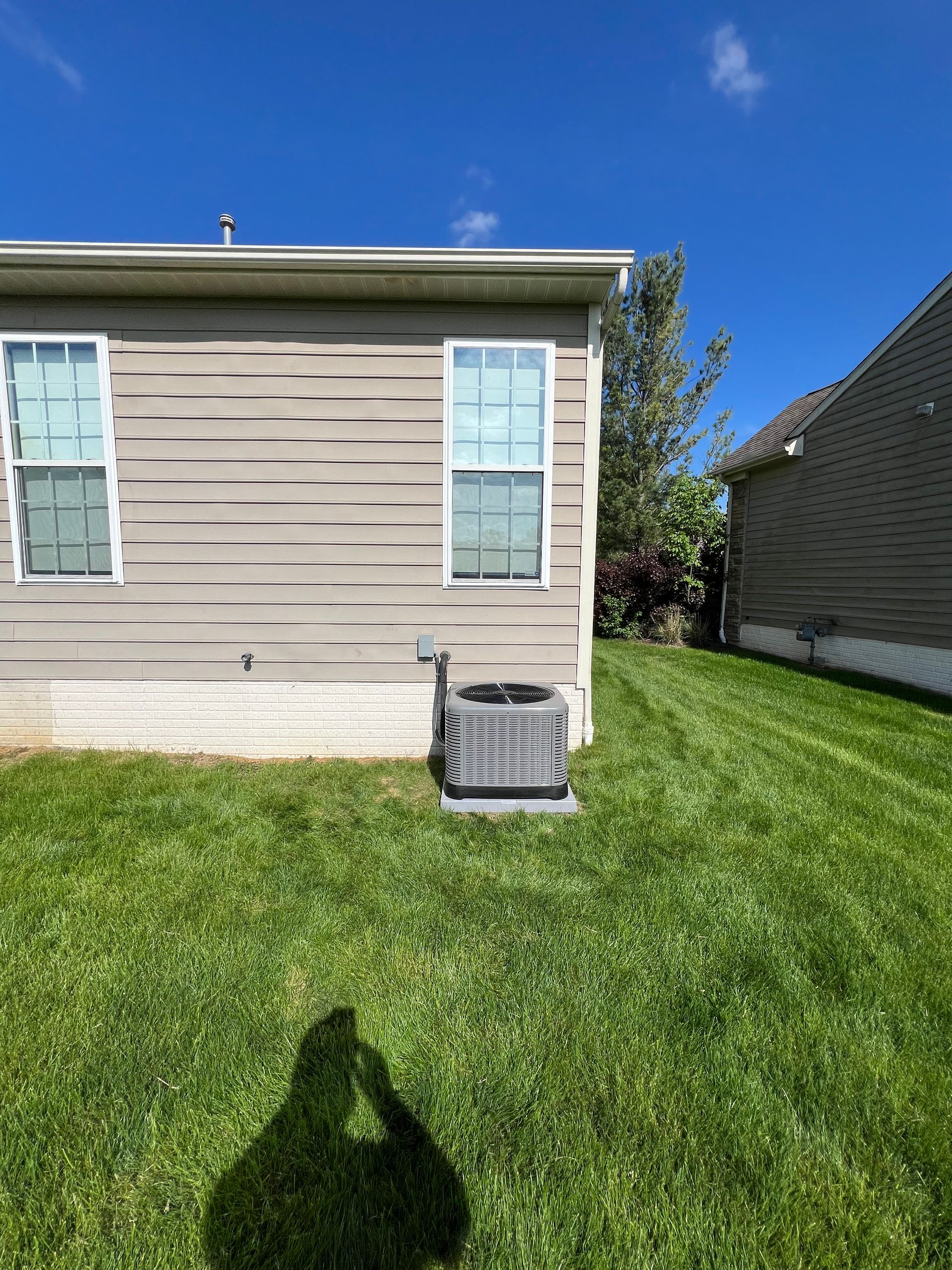 There is a shadow of a person on the grass in front of a house.
