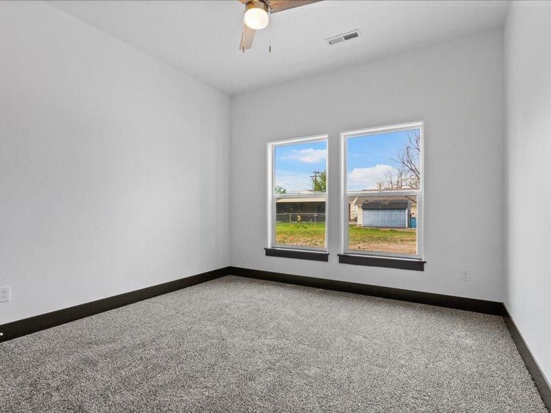 An empty bedroom with two windows and a ceiling fan.