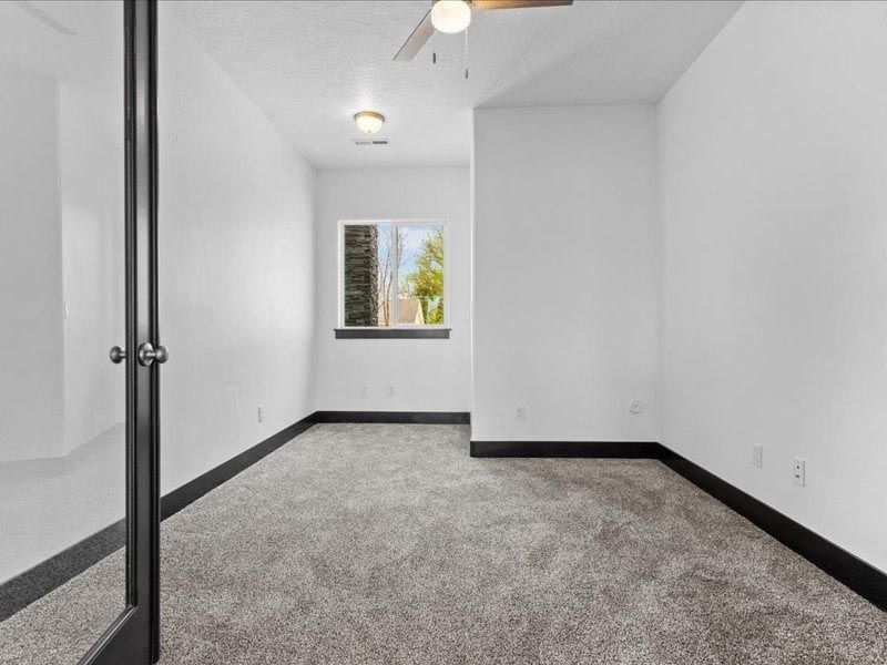An empty room with a ceiling fan and a window.