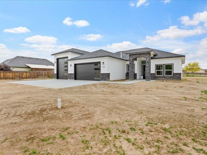 A white house with a black garage door is sitting on top of a dirt field.