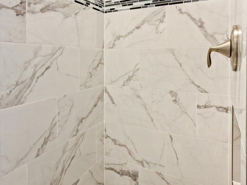 A shower with marble tiles and a stainless steel shower head.