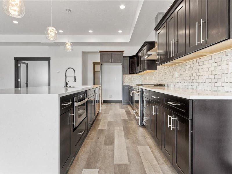A kitchen with wooden floors , black cabinets , stainless steel appliances and a large island.