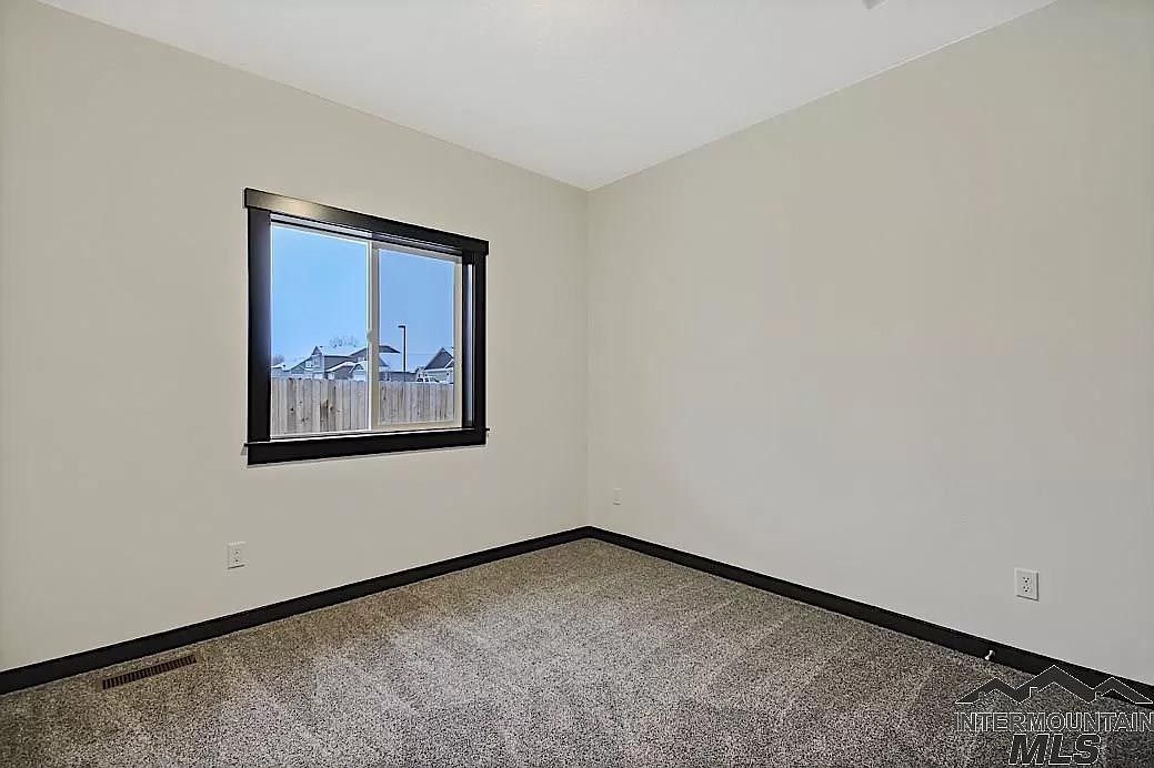 An empty bedroom with a window and a carpeted floor.