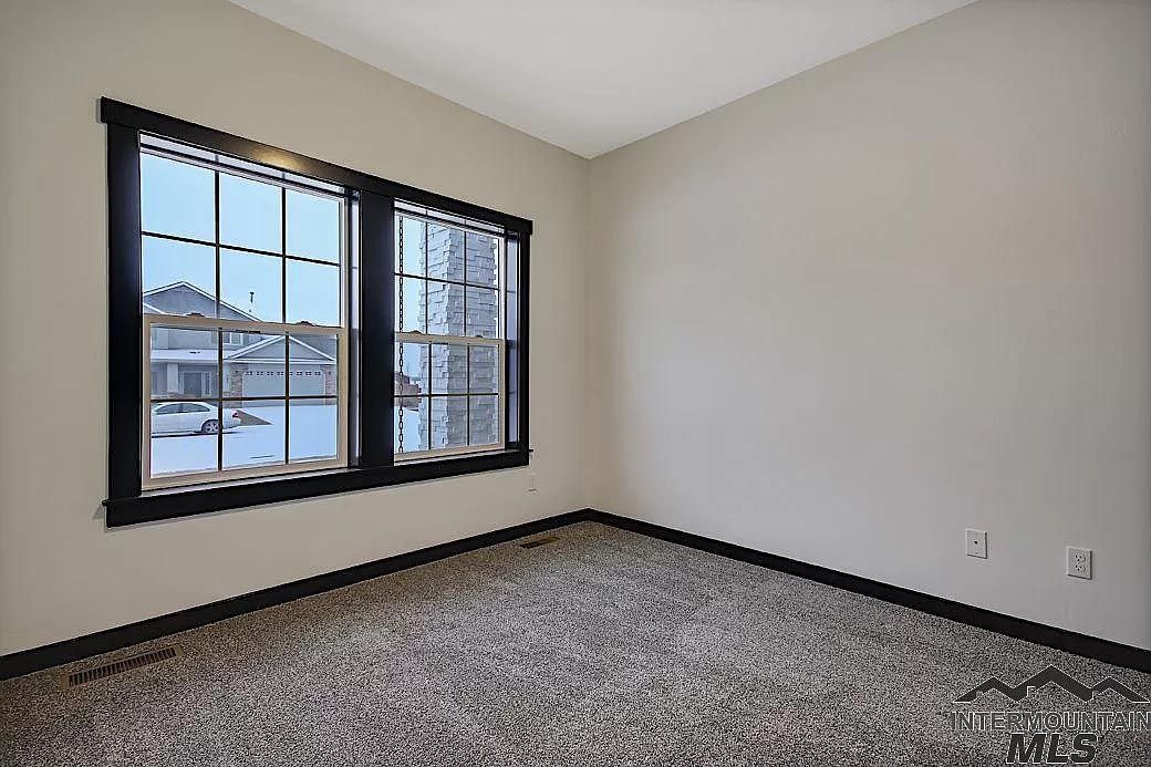 An empty bedroom with two windows and a carpeted floor.