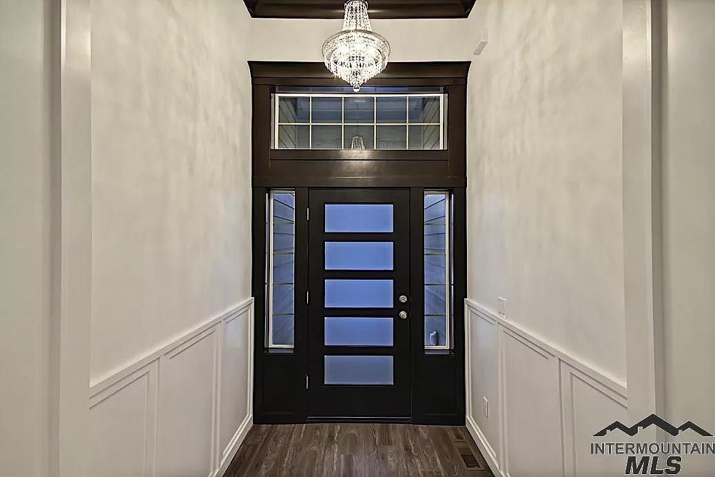 A hallway with a black door and a chandelier hanging from the ceiling.