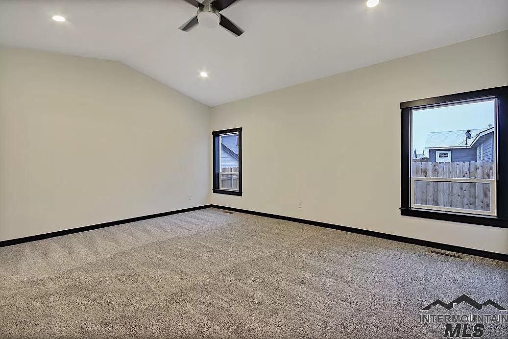 An empty bedroom with a ceiling fan and two windows.