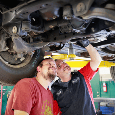 Service advisor and technician inspecting undercarriage of a car on a lift in a garage.