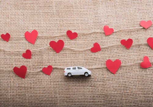 Van on a burlap background, surrounded by red paper hearts on strings.
