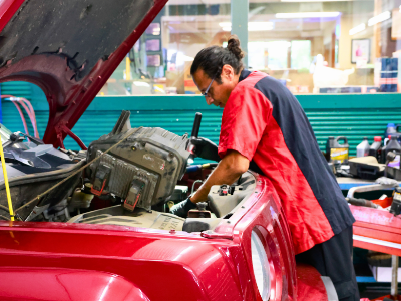 Jose inspects car engine with a flashlight in a garage.