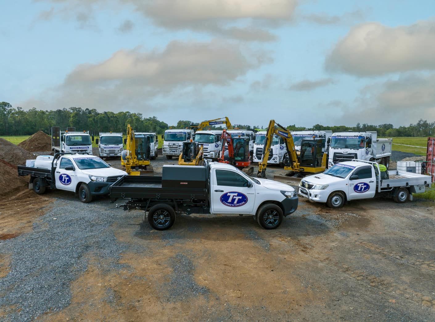 A Group Of Construction Trucks Are Parked In A Gravel Lot — Tymmo's In West Ballina, NSW